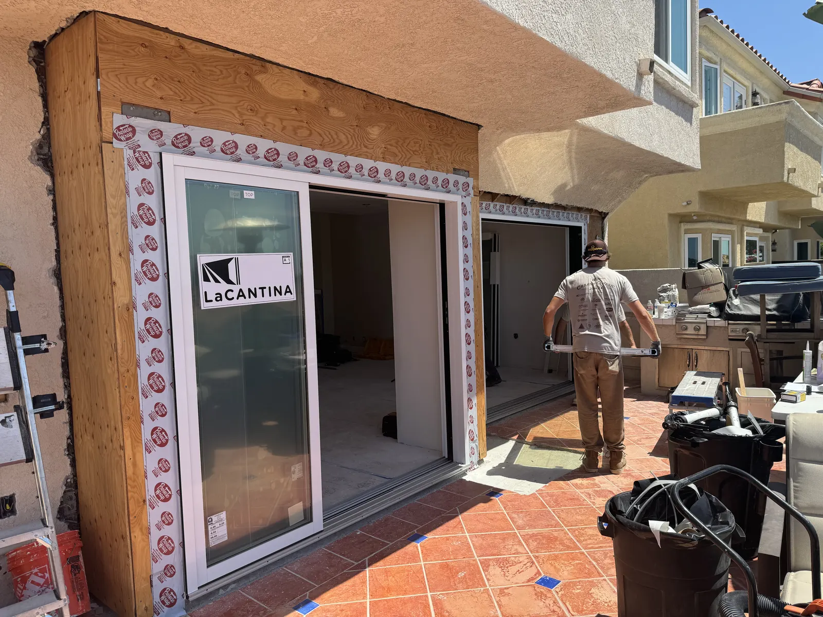 Before: exterior wall framed with exposed wood around a new glass door unit, with a crew member on the patio