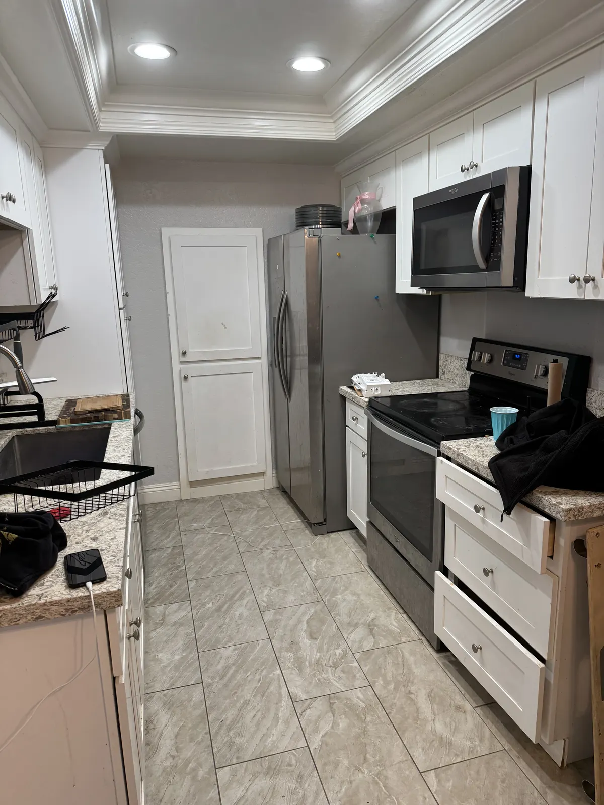 After: the same galley kitchen with white cabinets, stainless appliances and a new tile floor