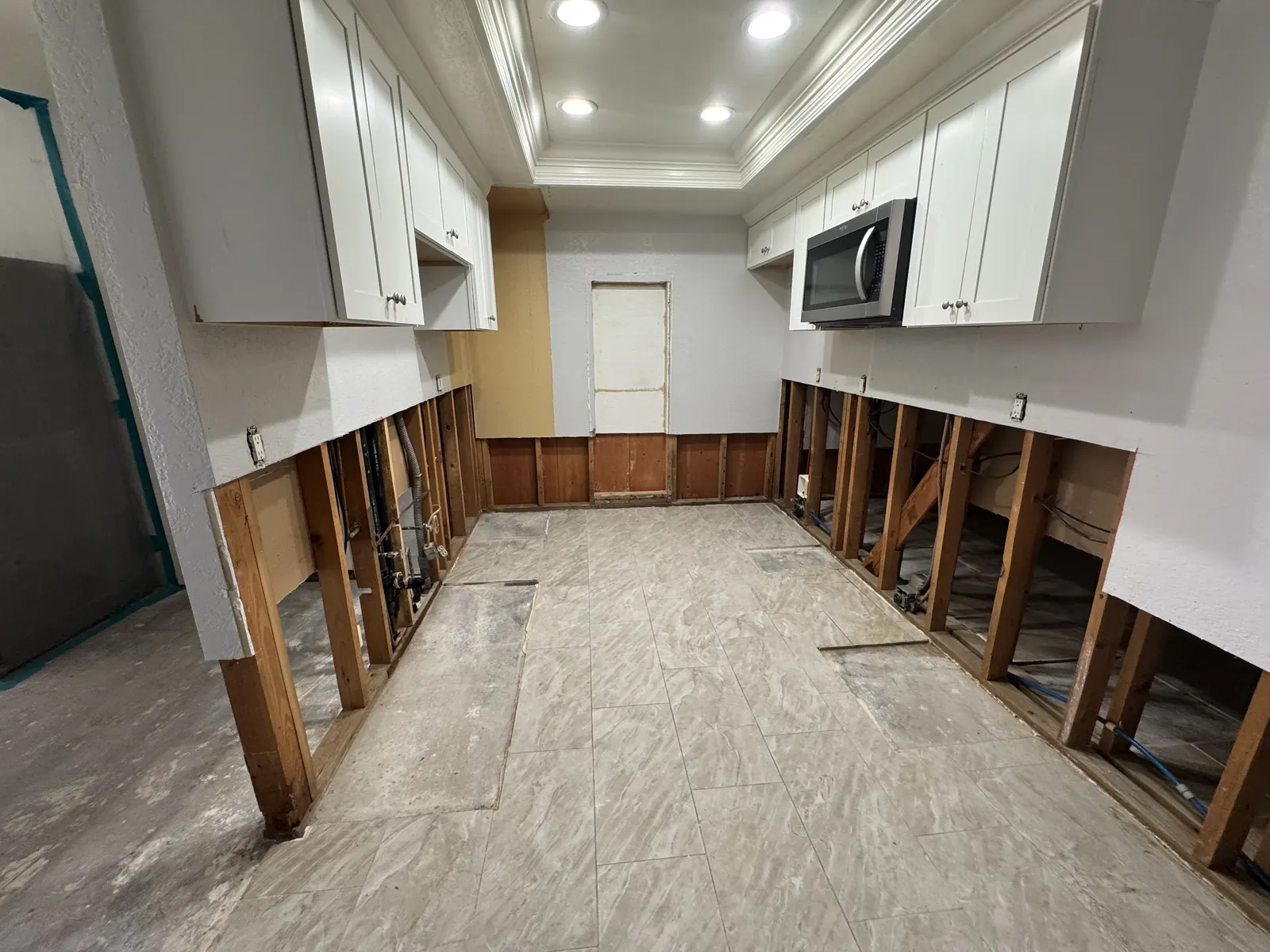 Before: galley kitchen with the lower drywall cut away, exposing wall studs below the cabinets