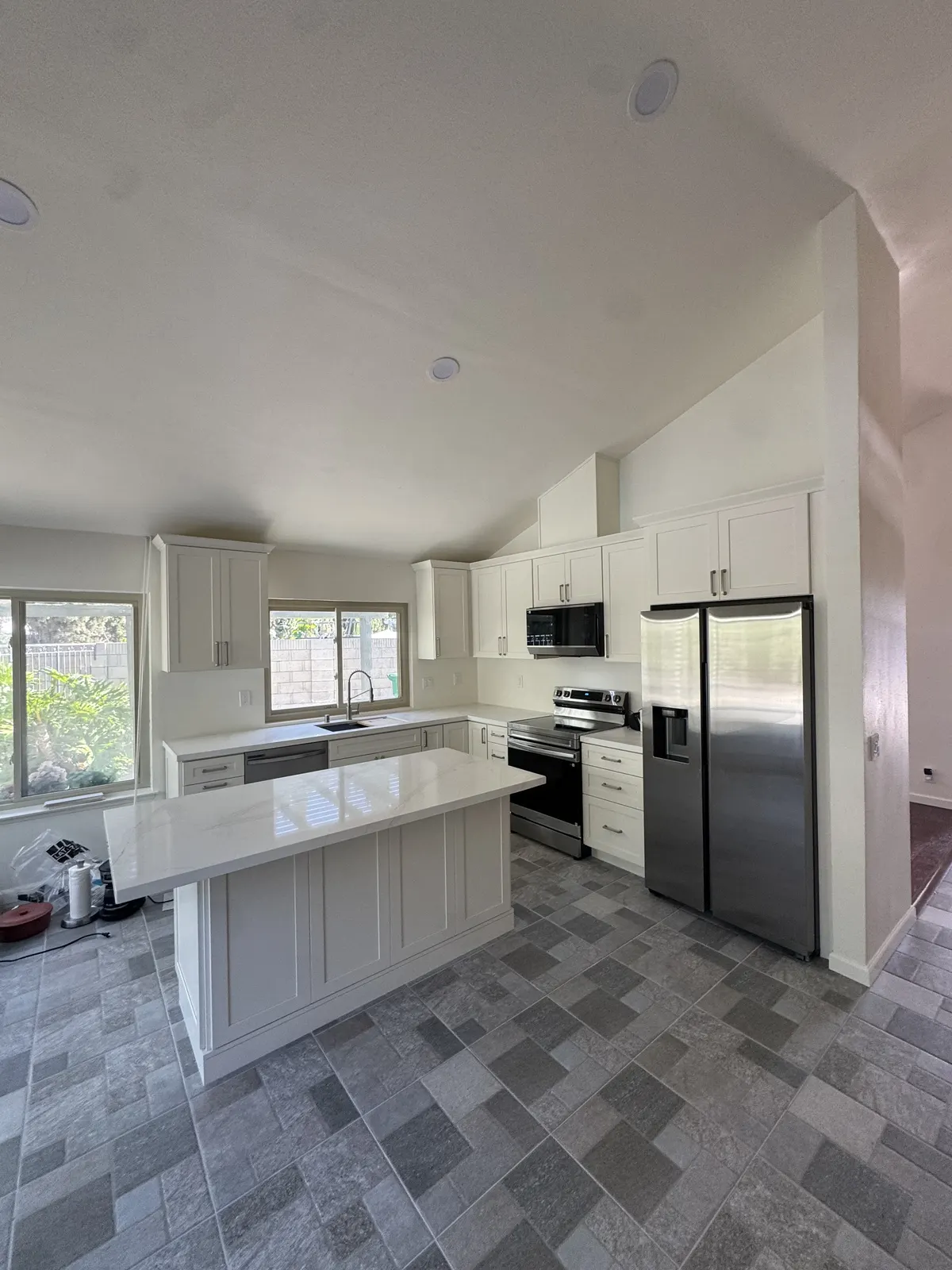 After: the same kitchen with white shaker cabinets, a white island countertop and new gray plank-pattern flooring