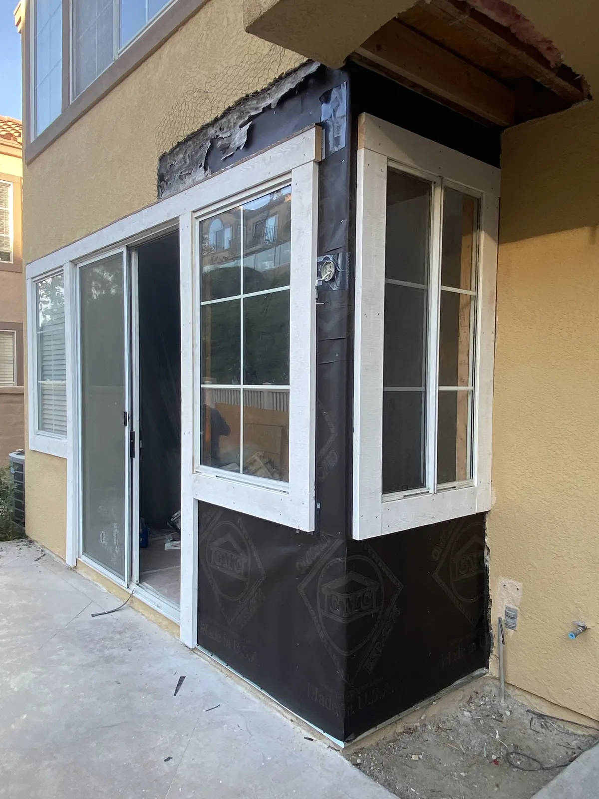 Exterior bay window and door section wrapped in black weather barrier before finishing