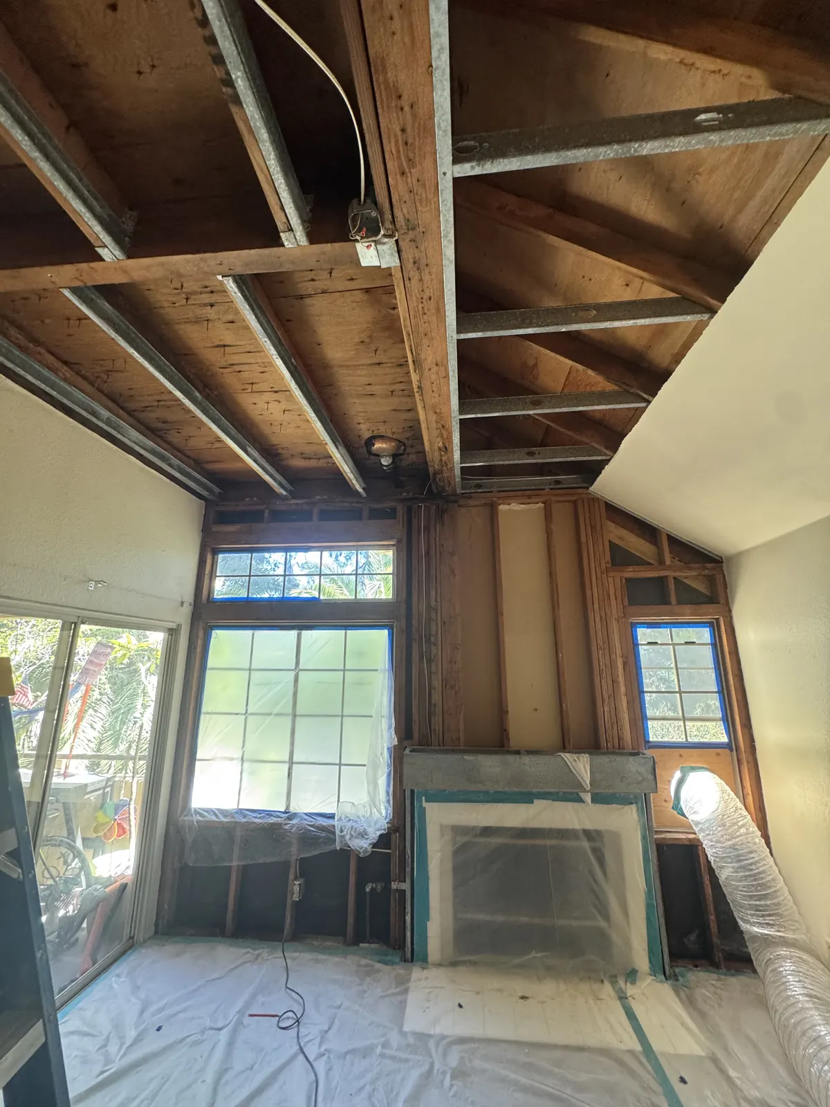 Room with the ceiling and upper walls opened to the framing and the floor covered in plastic