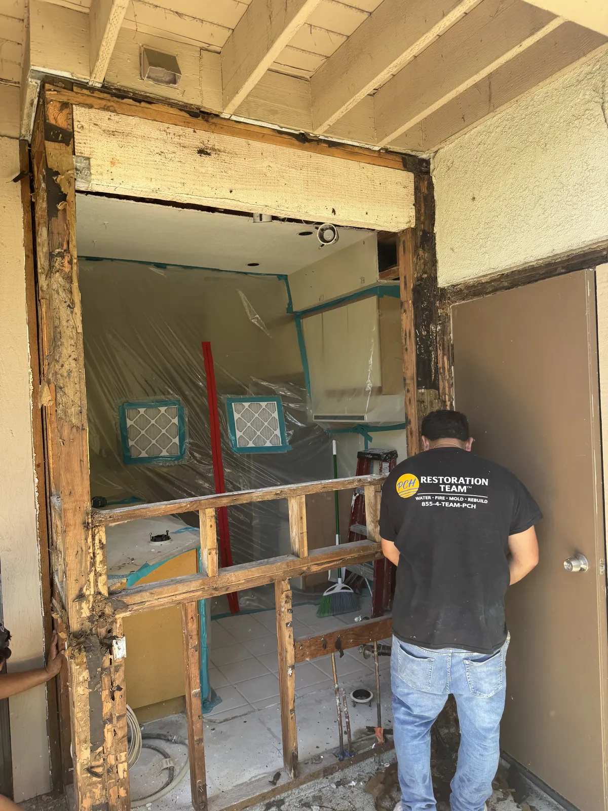 Crew member at an opened doorway with damaged wood framing around the opening