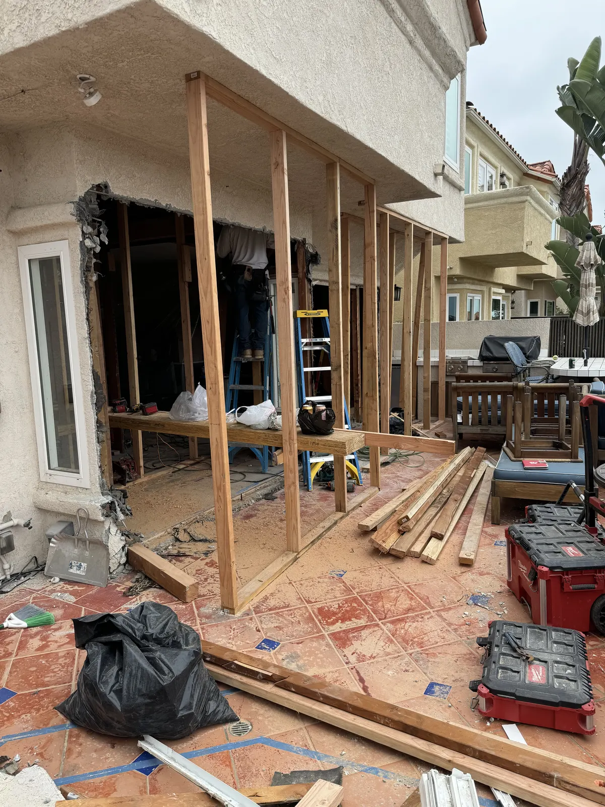 New wood wall framing built out over a tiled patio, with lumber and tools nearby