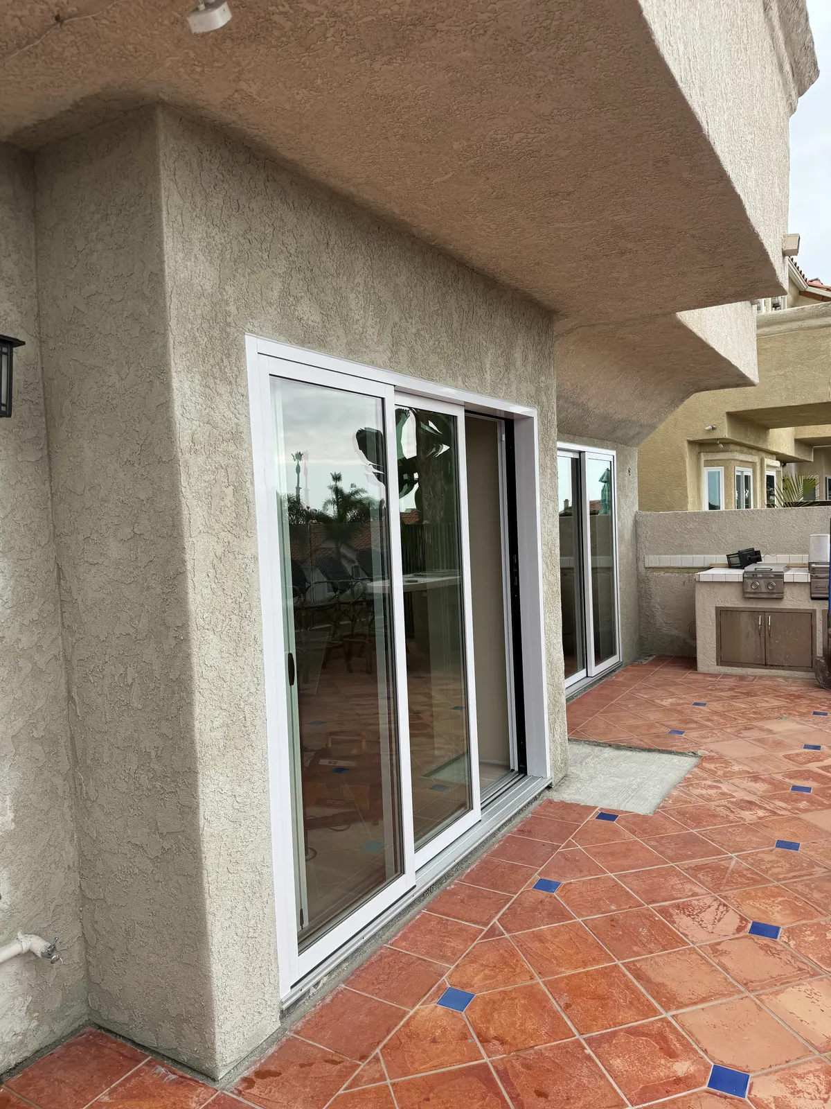 Exterior wall with new sliding glass doors and fresh stucco over a tiled patio