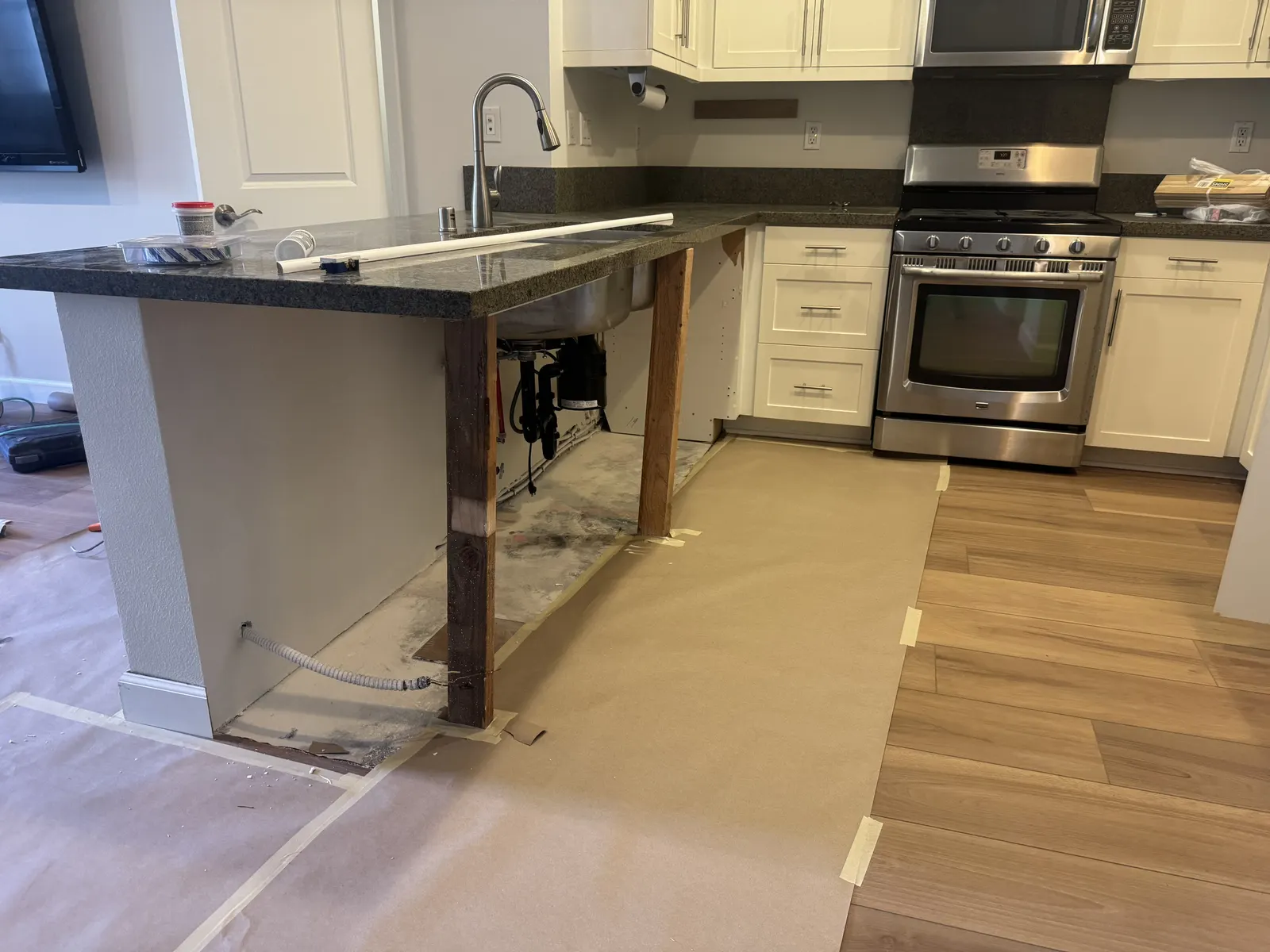 Kitchen island under construction with the countertop set and the base still open, next to new plank flooring