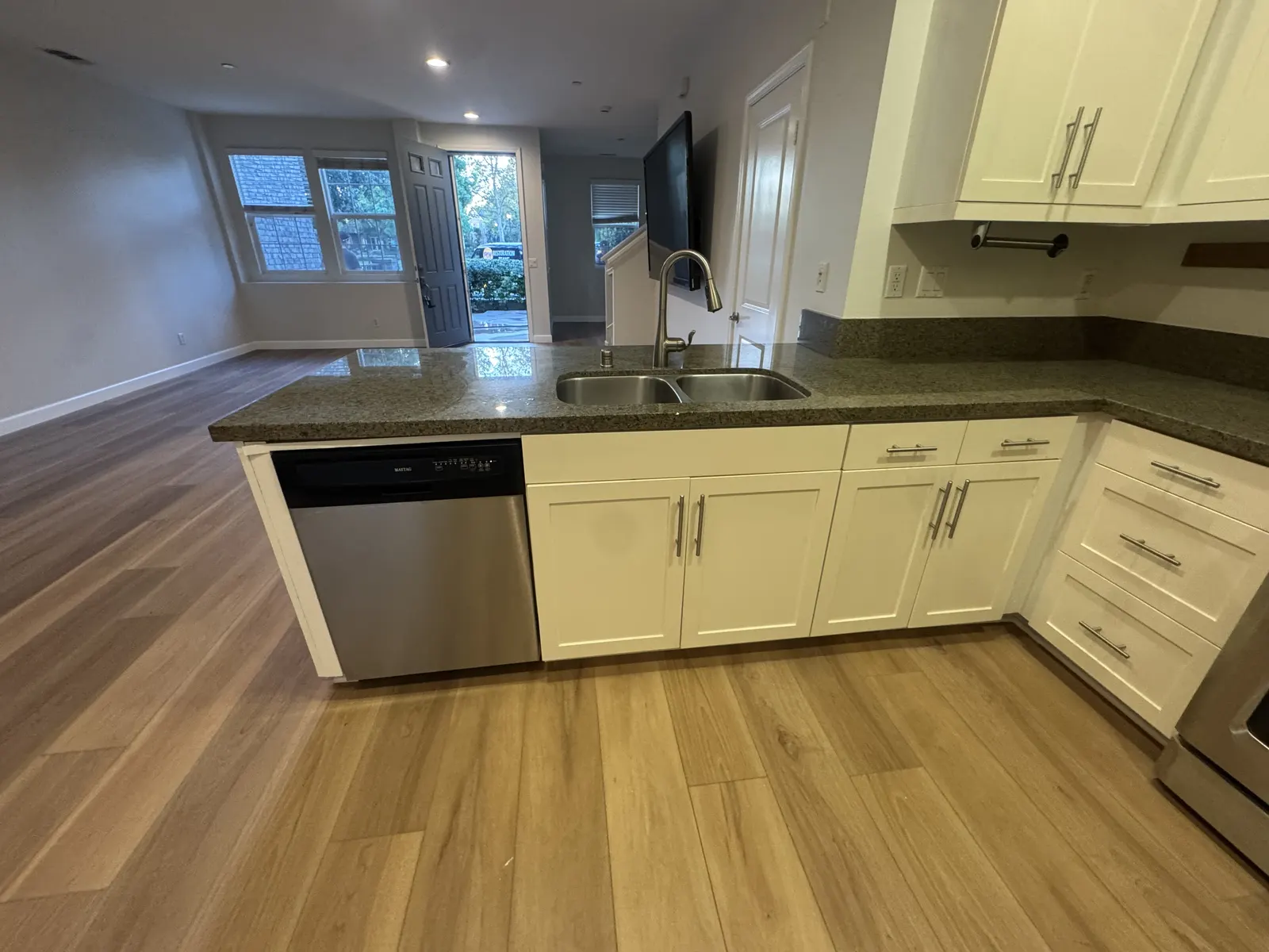 Finished kitchen with white cabinets, dark countertops and light wood-look plank flooring after reconstruction