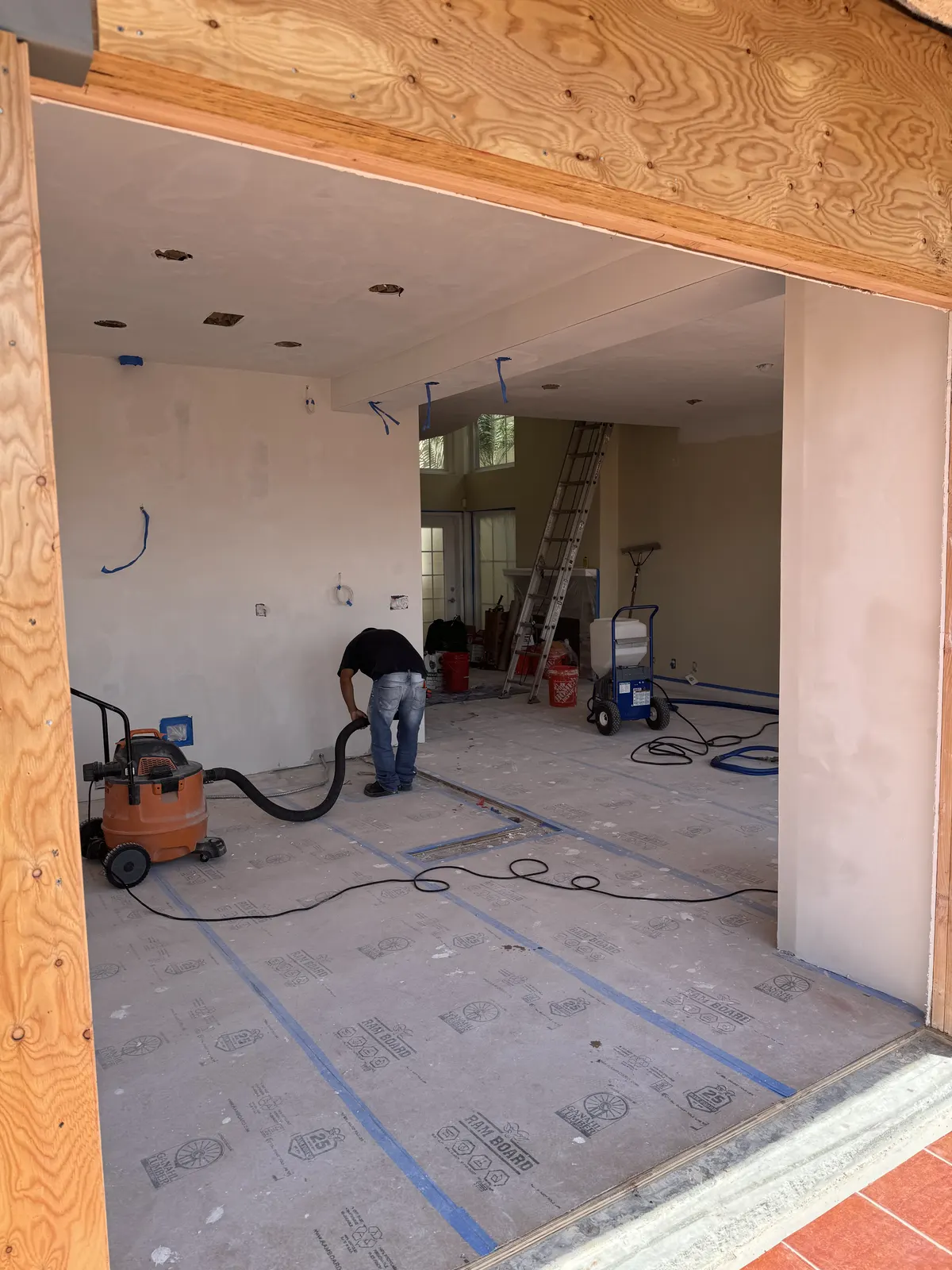 Interior room in progress with protected floors and a crew member using a shop vacuum