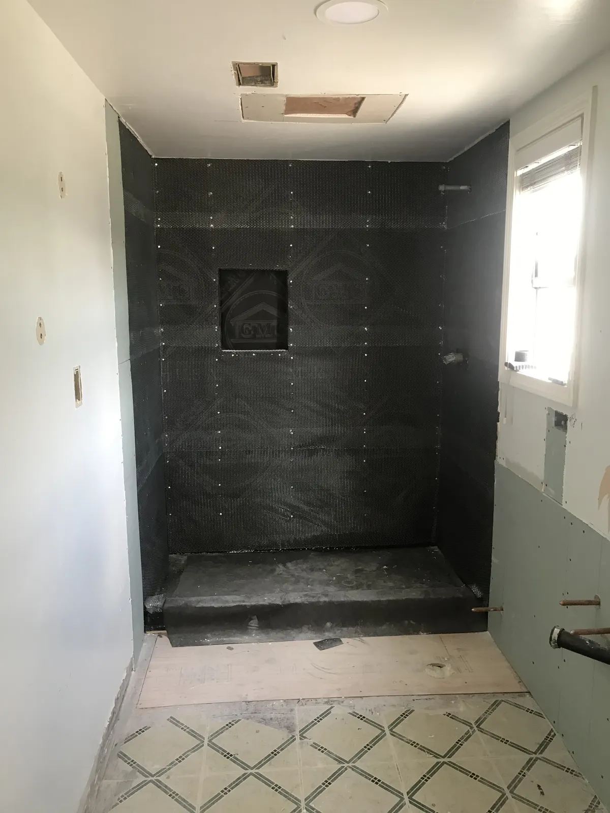 Shower enclosure covered in a dark waterproofing membrane with a recessed niche, before tile