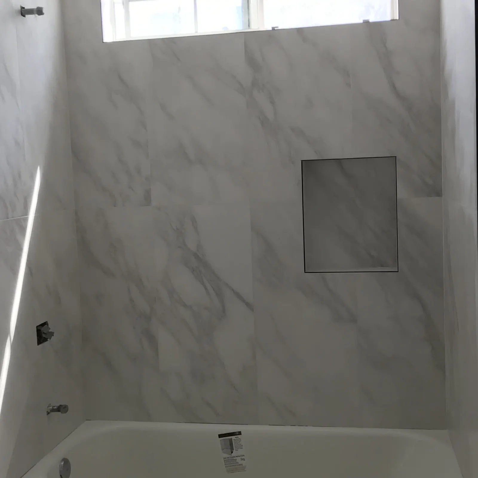 New bathtub surround in large marble-look tile with a recessed niche