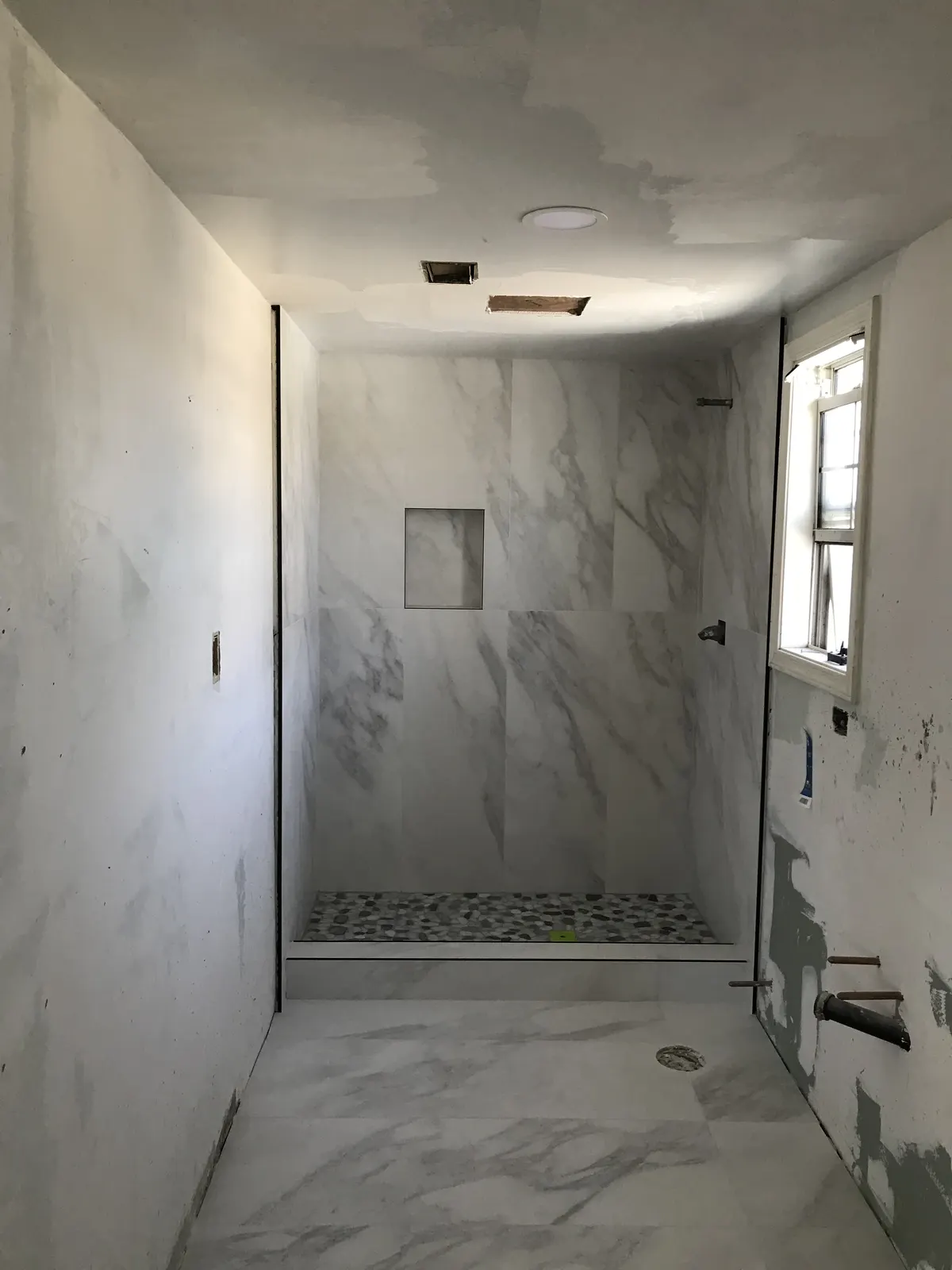 Walk-in shower finished in marble-look wall tile with a pebble floor and a recessed niche