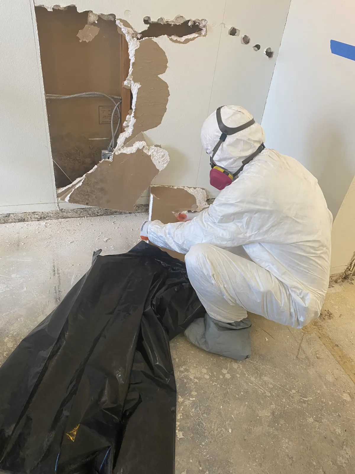 Technician in a protective suit and respirator bagging removed drywall