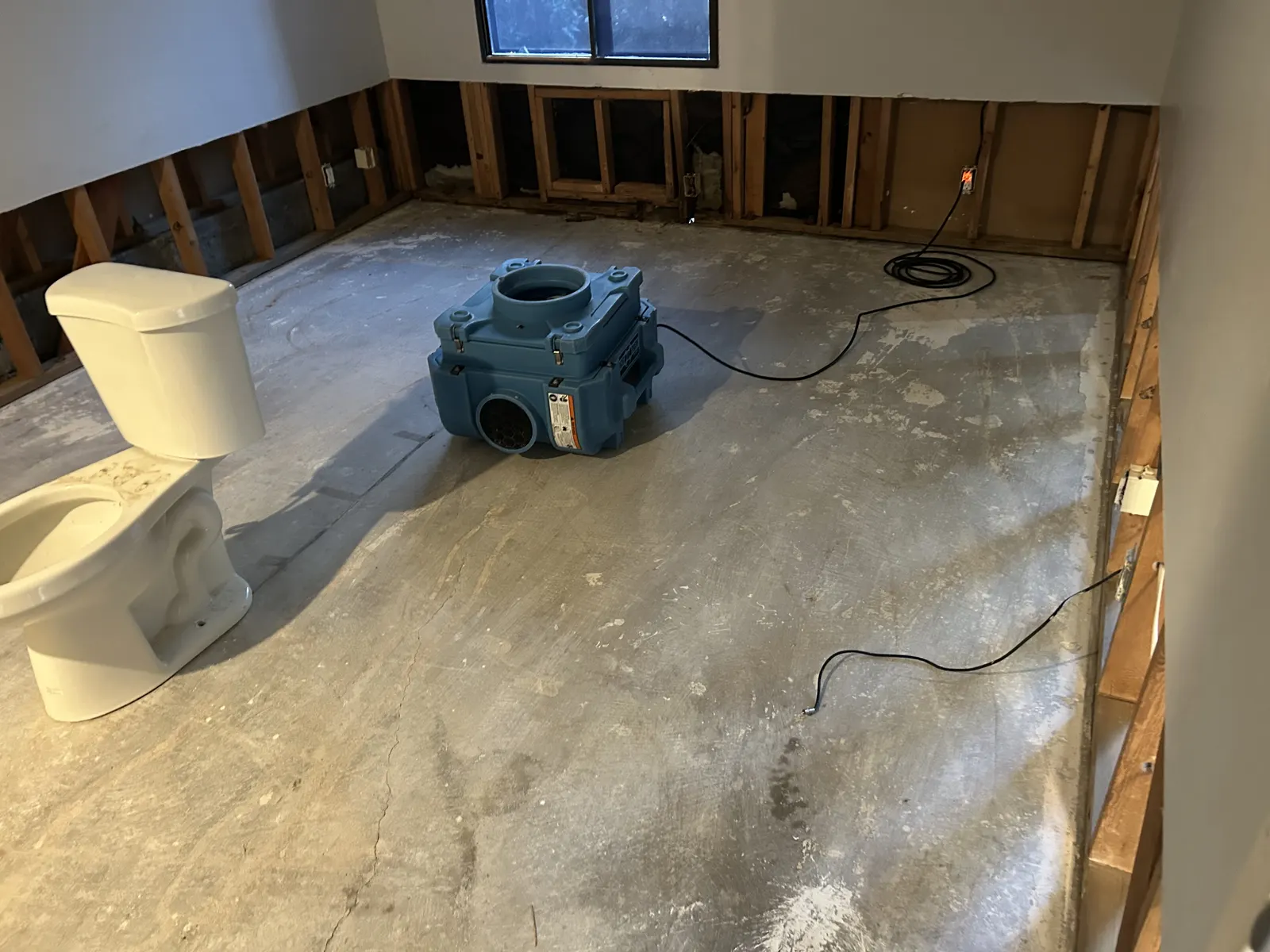 Bathroom with flooring and lower drywall removed, the toilet set aside and an air mover running