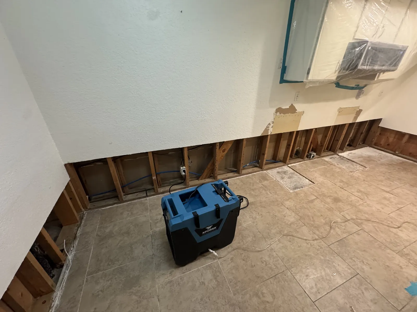 Room with the lower drywall cut away along the walls and a dehumidifier on the floor