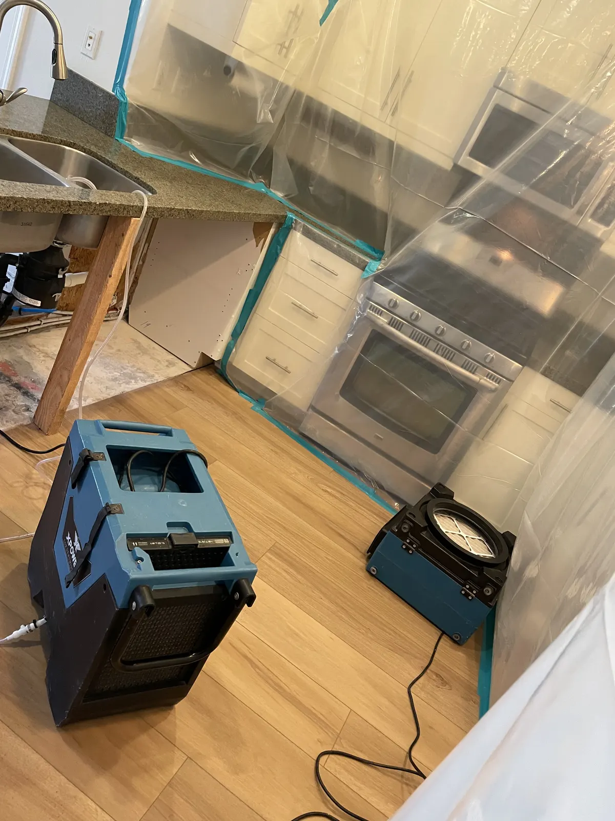 Kitchen with plastic sheeting over the cabinets and a dehumidifier and air mover on the floor