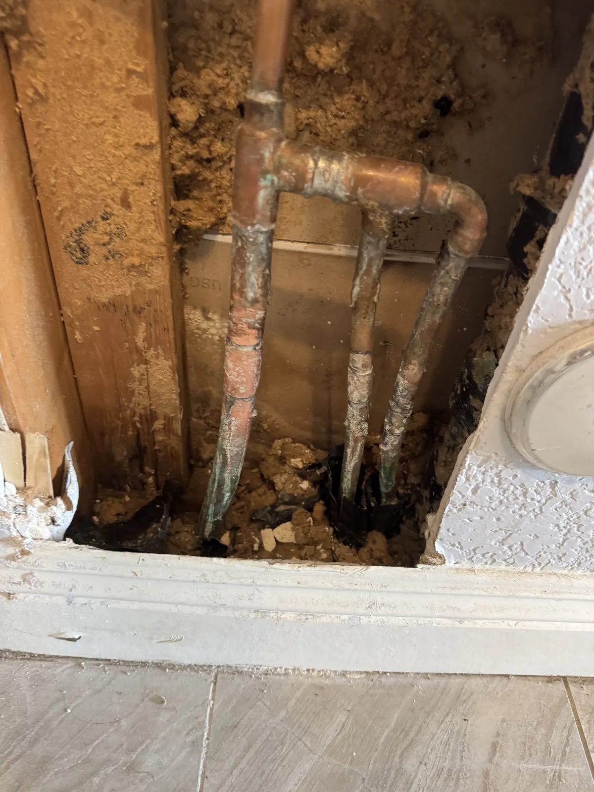 Section of wall opened at floor level exposing copper water pipes