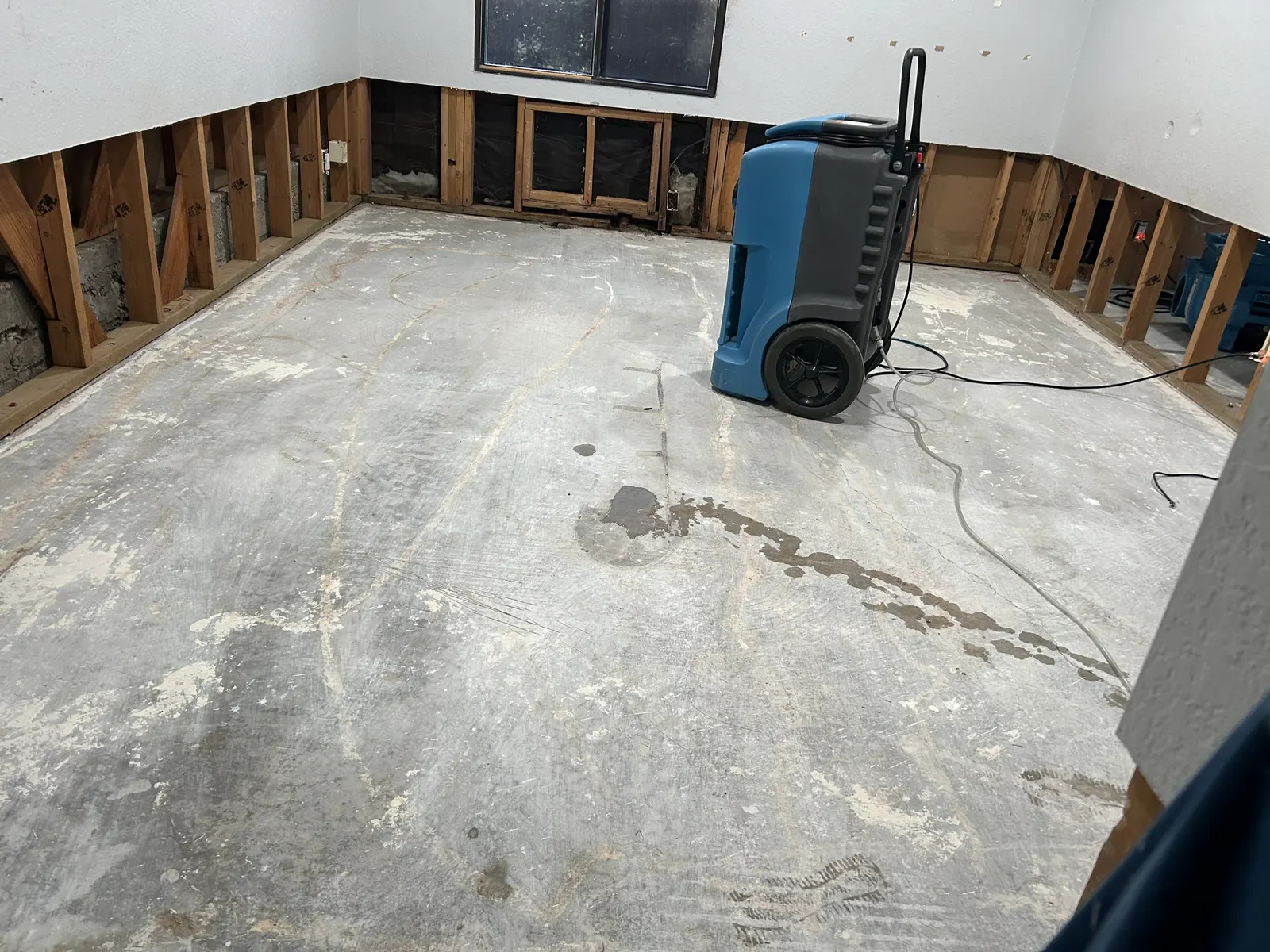 Empty room with flooring removed, lower walls opened and a dehumidifier running
