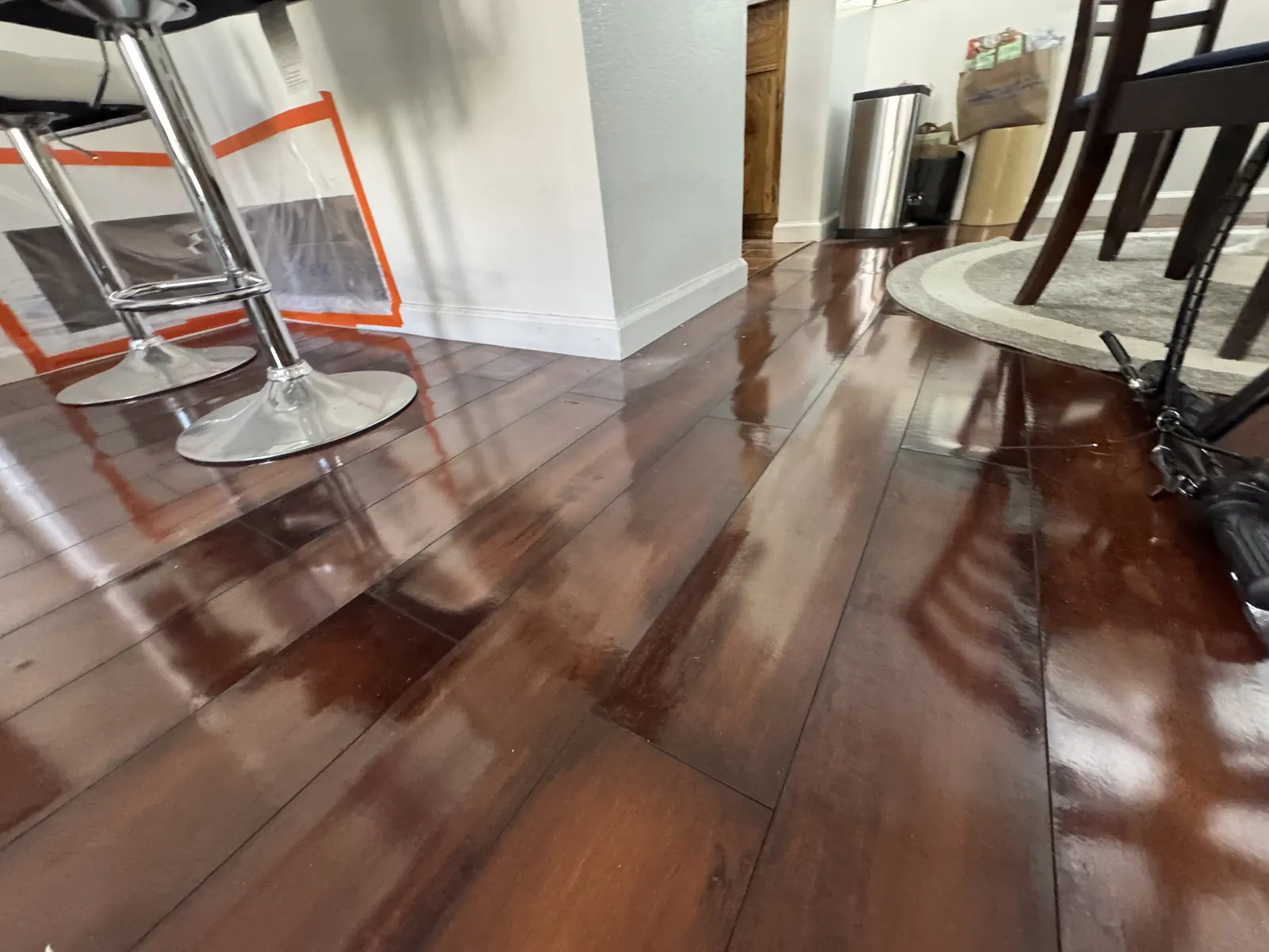 Standing water across a wood-look floor under bar stools and a dining table