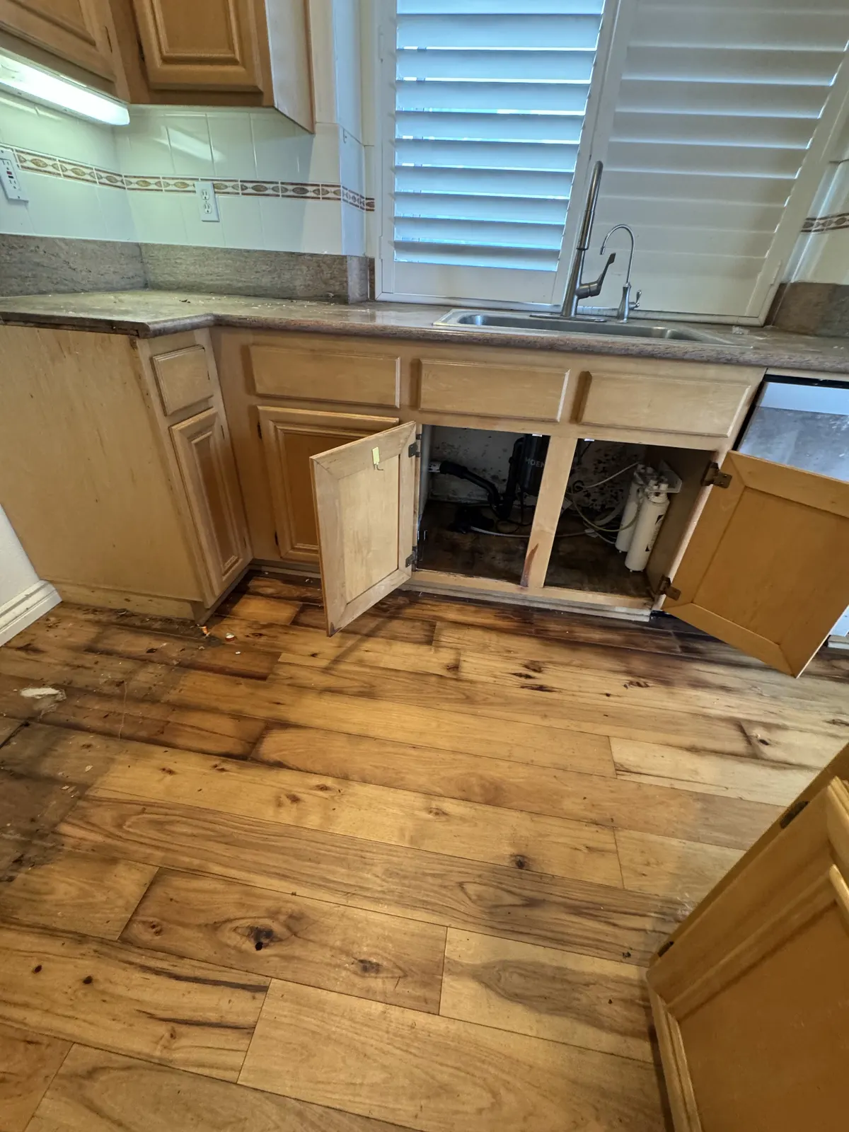 Dark water stains on a wood floor in front of an open sink cabinet