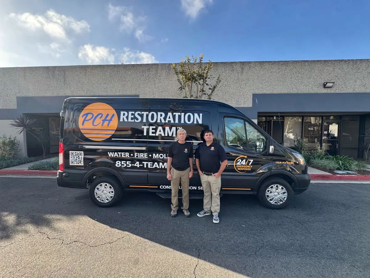 Two PCH Restoration Team members in company shirts standing beside a branded PCH van outside the team's Laguna Hills shop