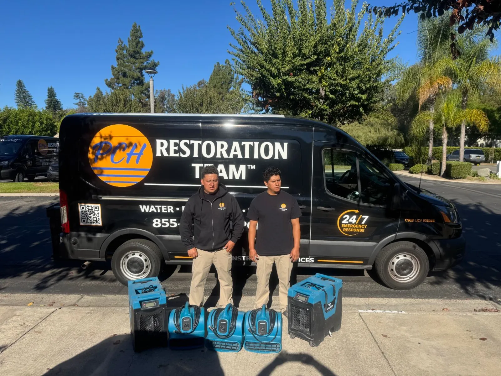 Two PCH Restoration Team technicians with dehumidifiers and air movers in front of a branded PCH response van in Orange County, California