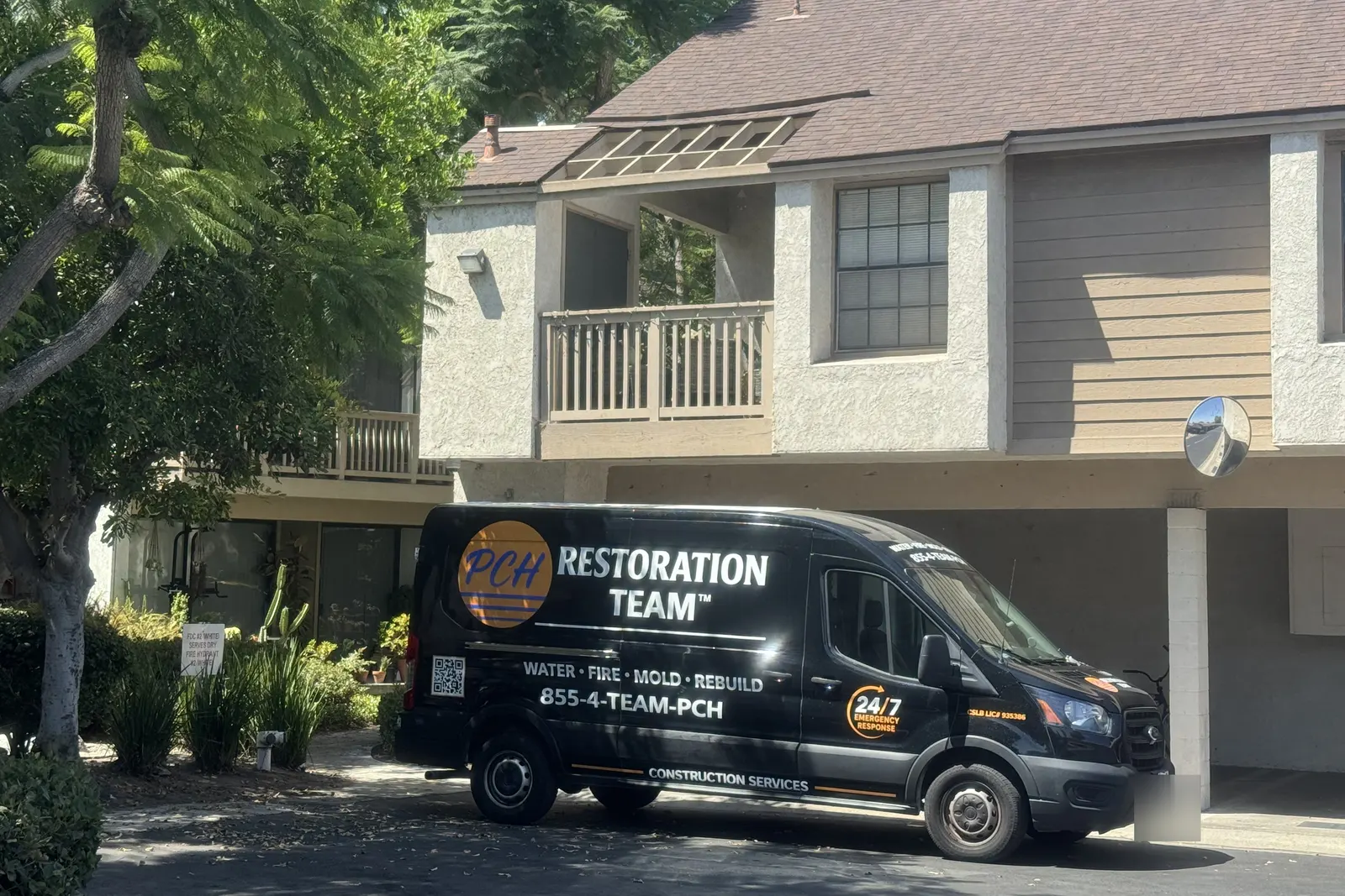 PCH Restoration Team response van parked at a two-story multi-unit building with carport parking
