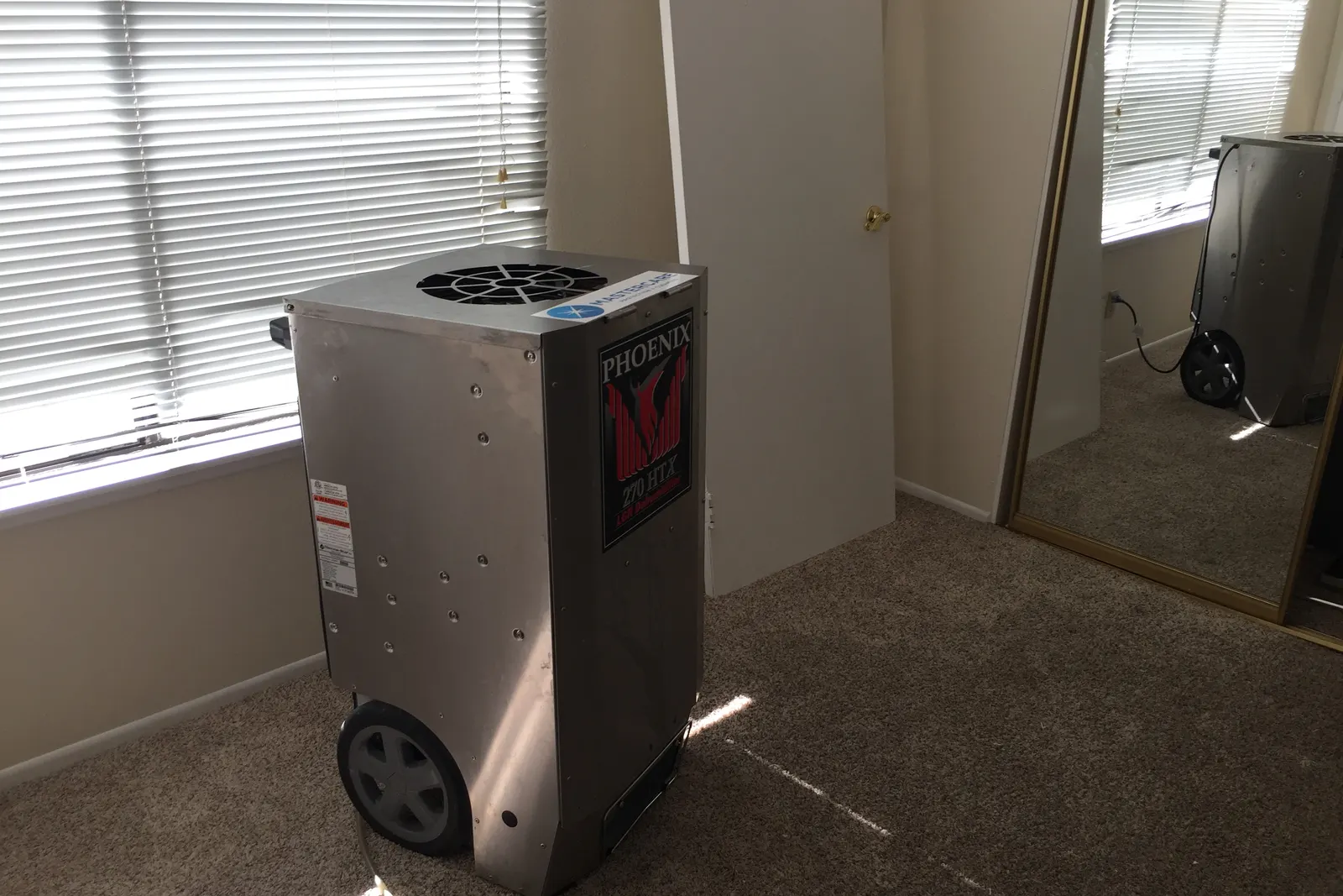 Commercial dehumidifier drying a carpeted bedroom during residential water damage restoration
