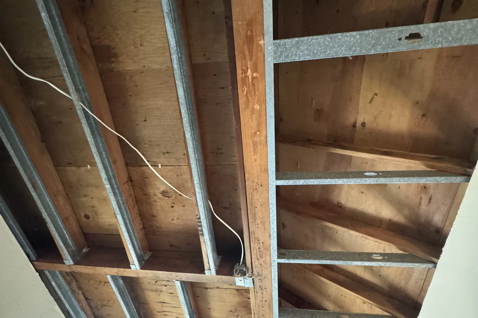 Ceiling opened to the joists and roof decking after a roof leak, with a window below
