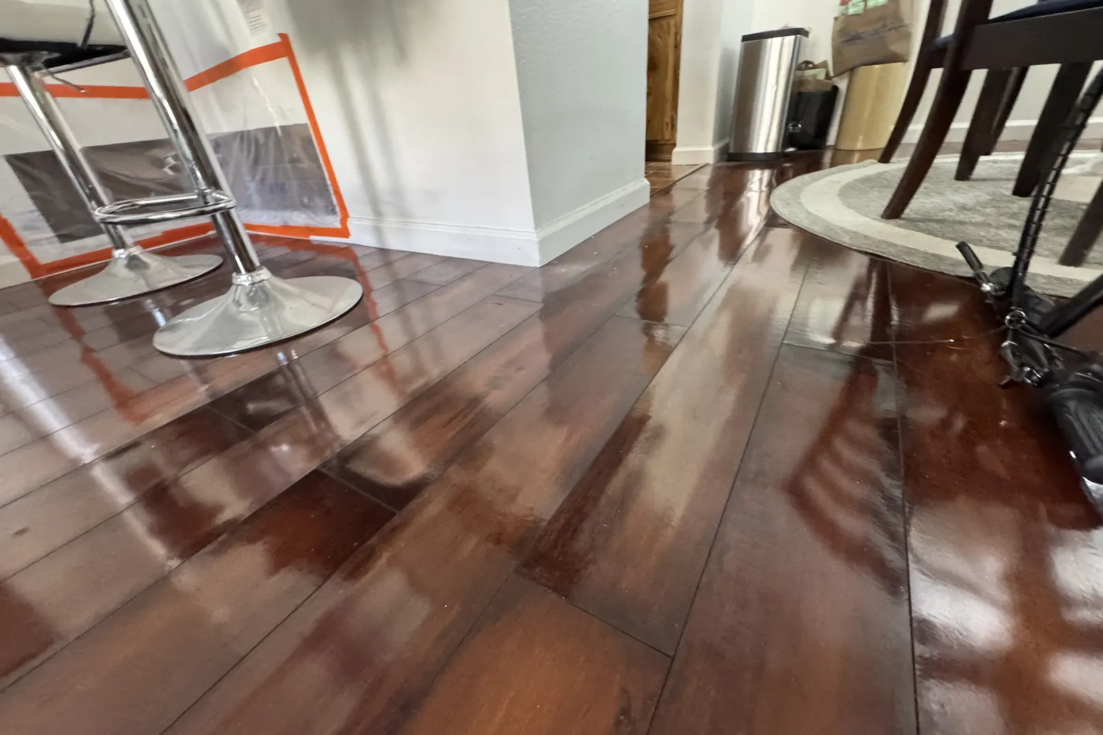 Standing water across a hardwood floor under bar stools and dining chairs before emergency water removal