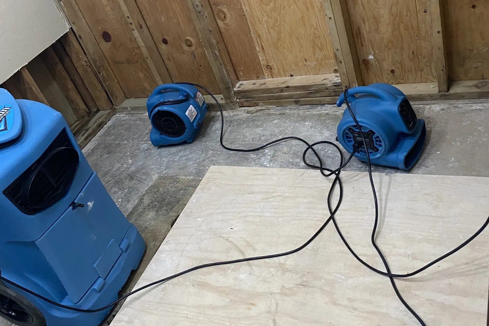 Air movers and a dehumidifier drying exposed wall sheathing and subfloor during structural drying