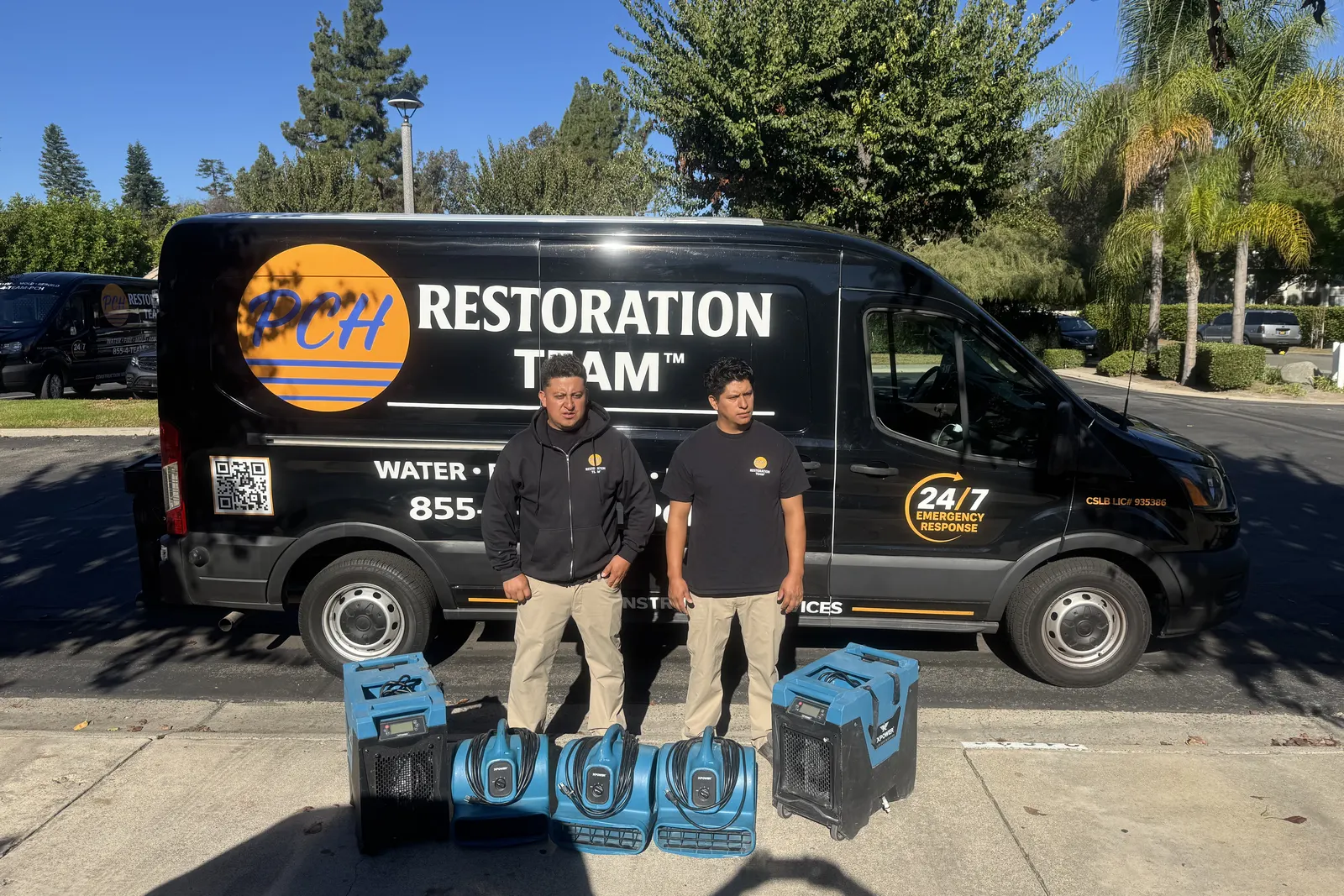 Two PCH Restoration Team technicians with air movers and dehumidifiers lined up beside a response van